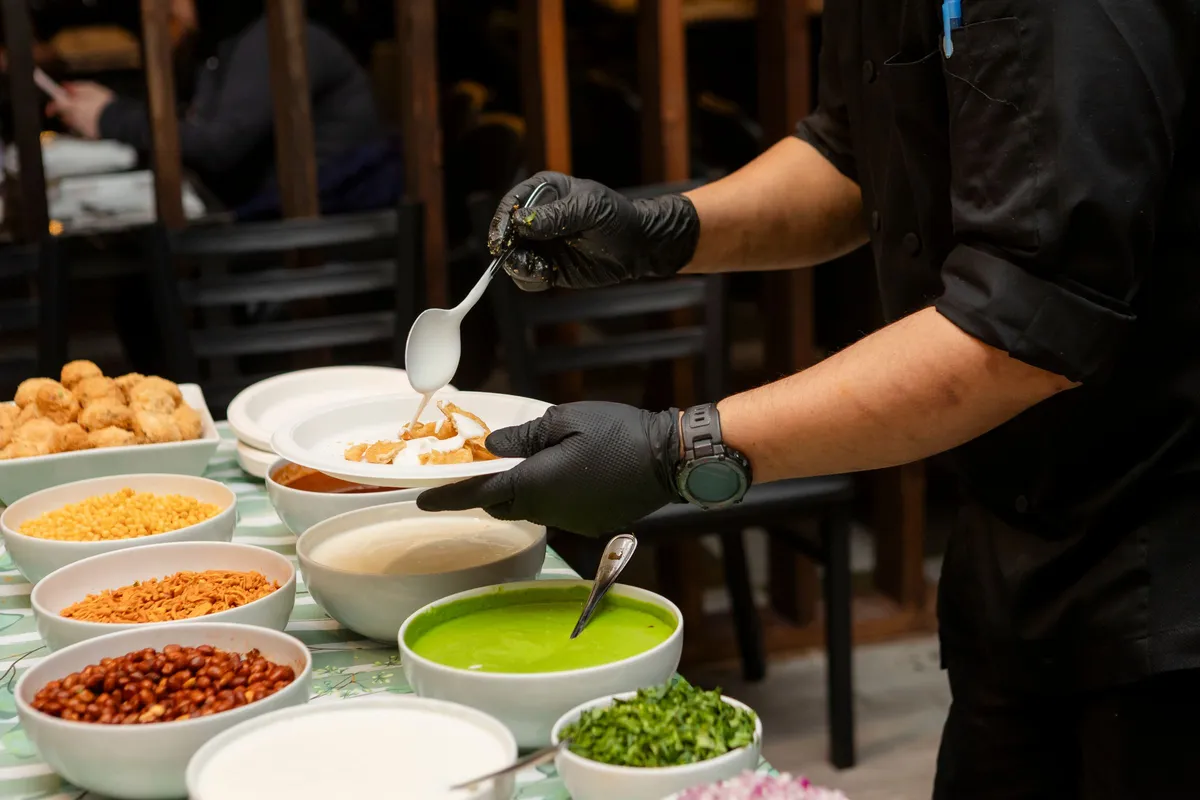 Gloved chef's hands plating Indian chaat with chutneys and toppings arranged in bowls