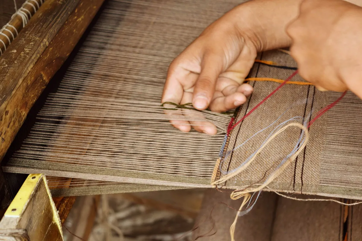 Close-up of a weaver's hands passing thread across the warp on a traditional wooden handloom