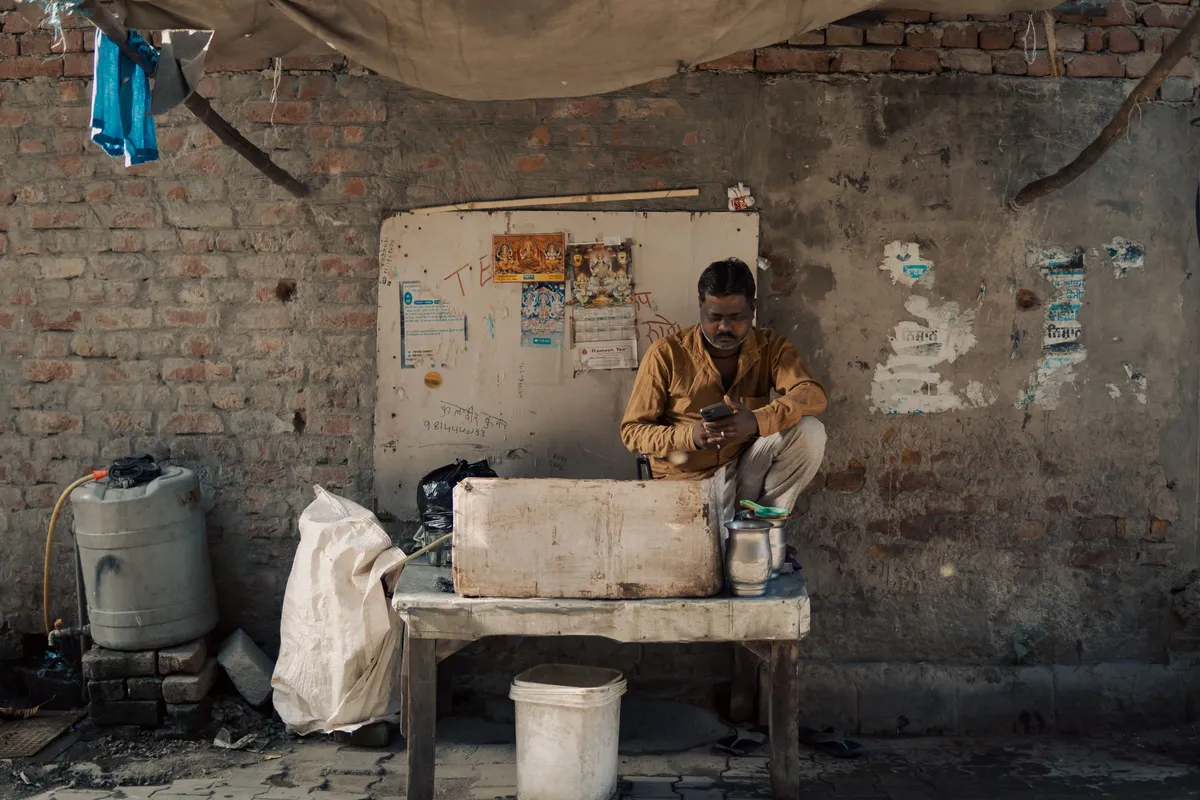 Indian street vendor sitting at his work table and checking messages on a mobile phone